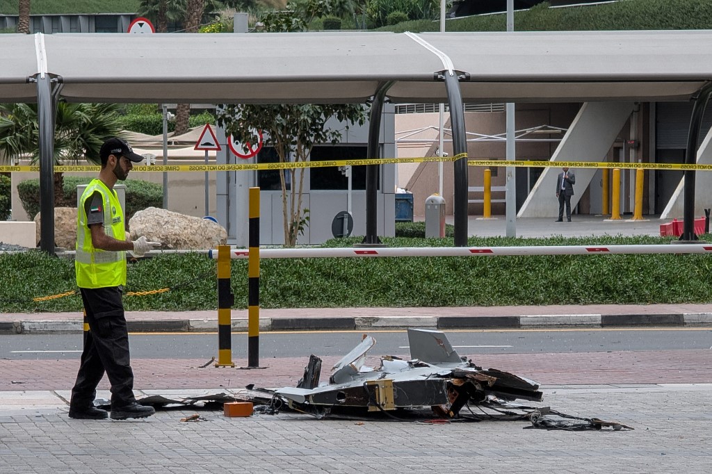 A policeman inspects the wreckage of a drone in downtown Dubai on March 12, 2026. Dubai reported a drone attack and fallen debris in two locations on March 12, while Kuwait's airport was damaged in yet another strike on the facility during Iran's Gulf campaign in the Middle East war. (Photo by AFP) /